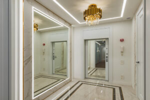 Velké podsvícené zrcadlo v luxusní předsíni je umístěné vedle vstupních dveří a rozjasňuje prostor.