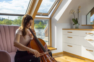 Dcera majitelů hraje na violoncello v prosluněném podkrovním pokoji s výhledem na střešní terasu.