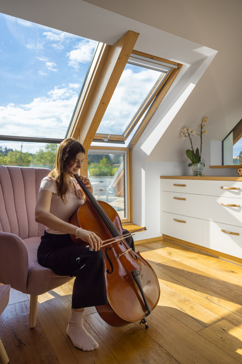 Dcera majitelů hraje na violoncello v prosluněném podkrovním pokoji s výhledem na střešní terasu.