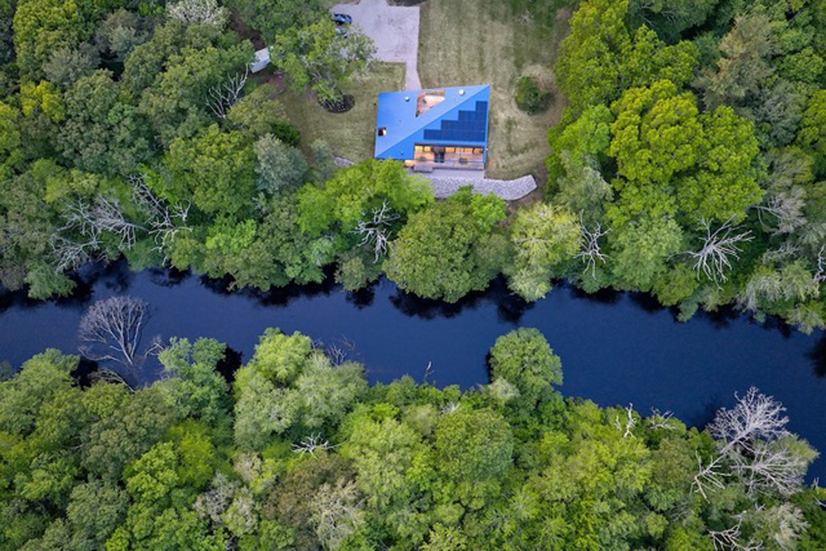 Letecký pohled na dům Riverhouse ukazuje jeho umístění v těsné blízkosti řeky a hustého lesa.