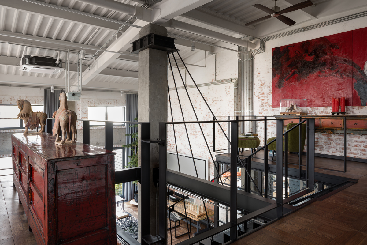 Horní galerie loftu propojuje surové betonové sloupy, černé ocelové konstrukce a starožitný nábytek v prostoru, který funguje zároveň jako soukromá zóna i domácí galerie.
