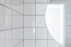 Bílé čtvercové obklady s tmavou spárou dodávají koupelně minimalistický, ale výrazný charakter inspirovaný středomořskou estetikou.