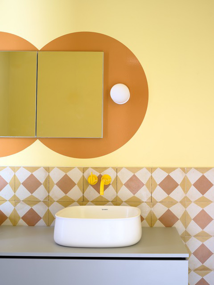 Barevně laděná koupelna v domě Riverhouse kombinuje pastelové tóny, geometrické obklady a minimalistické umyvadlo s hravými designovými detaily.