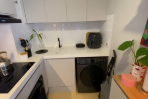 Moderní kuchyňská linka kombinuje vestavěné spotřebiče, pračku a minimalistický design v neutrálních barvách.