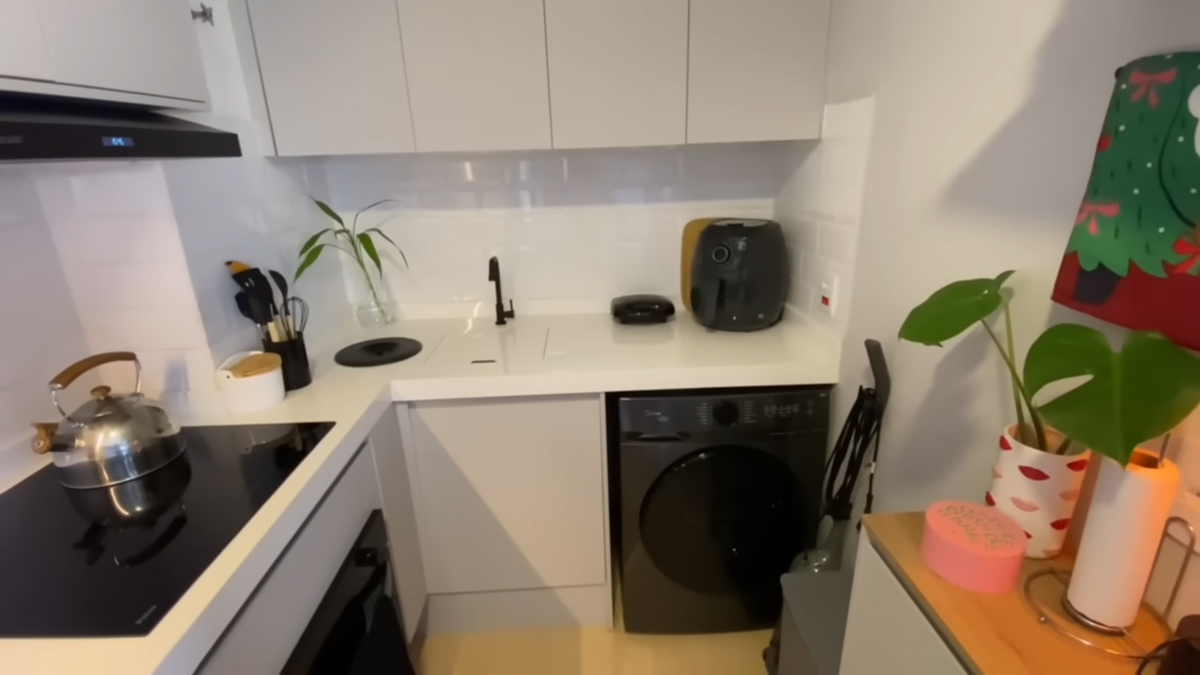 Moderní kuchyňská linka kombinuje vestavěné spotřebiče, pračku a minimalistický design v neutrálních barvách.