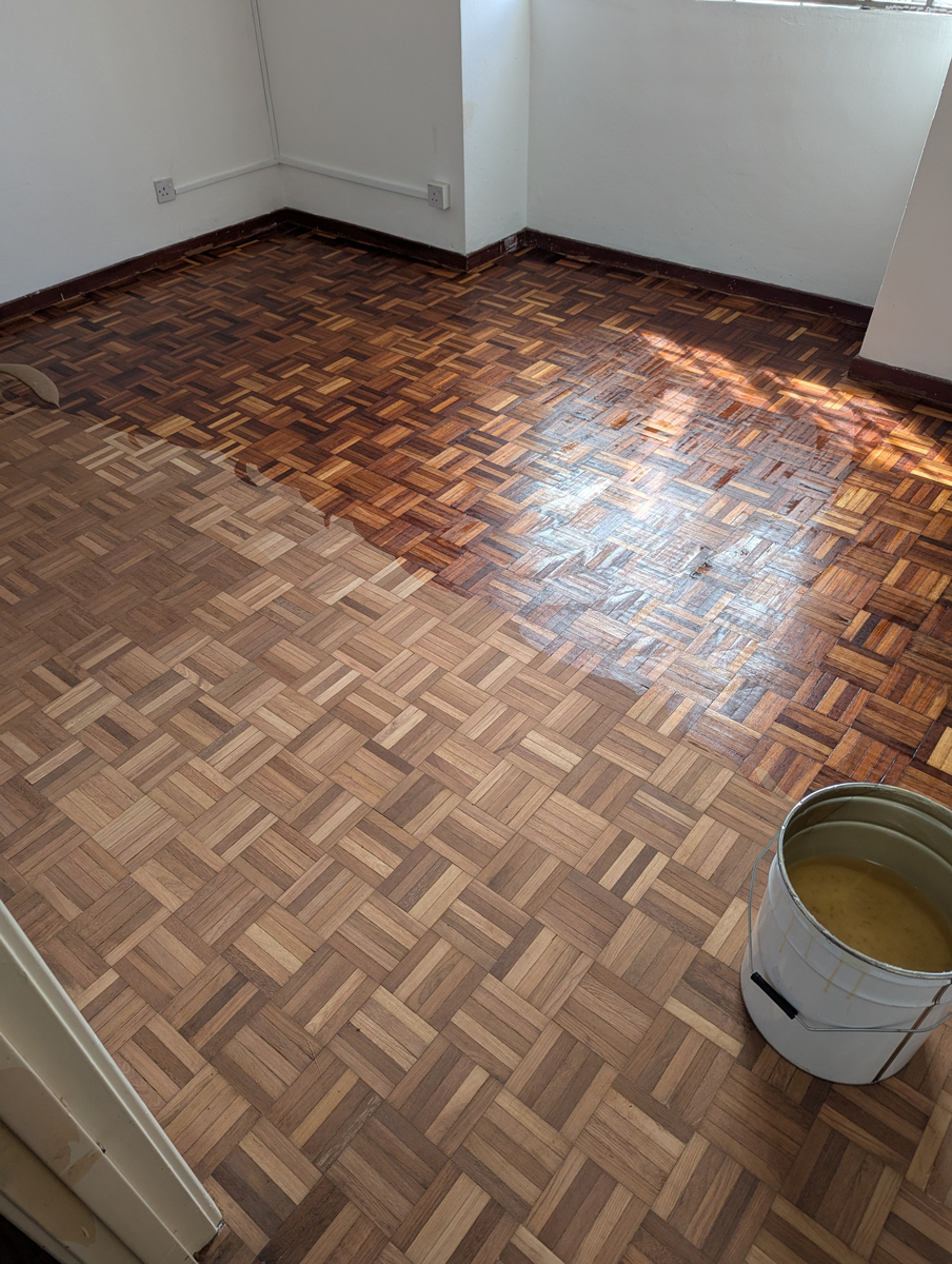 Renovace staré parketové podlahy ukazuje výrazný rozdíl mezi původním tmavým lakem a nově opravenou částí po broušení a nové povrchové úpravě.