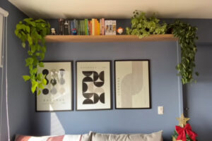 Tmavě modrá stěna s minimalistickými plakáty a policí plnou knih vytváří výrazný designový prvek obývacího pokoje.