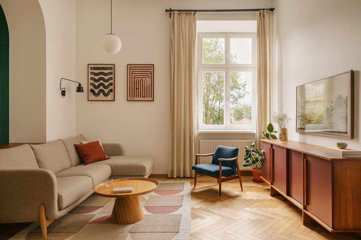 Obývací část s vysokými okny, dubovou podlahou a retro komodou propojuje historickou architekturu se současným designem.