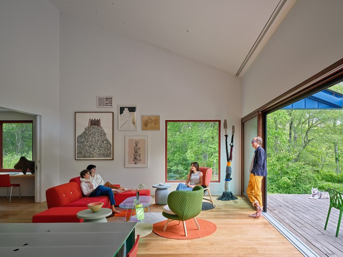 Hlavní obytný prostor domu Riverhouse propojuje minimalistický interiér s přírodou díky velkým posuvným oknům a otevřenému výhledu do zeleně.