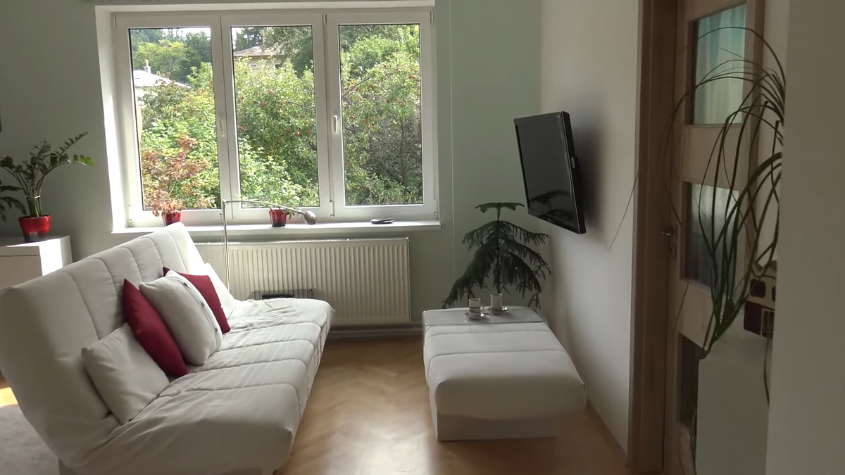Minimalistický obývací pokoj s futonovou pohovkou a velkým oknem působí vzdušně díky otevřené dispozici.