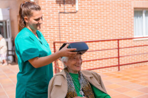 Zdravotnice pomáhá seniorce nasadit VR headset během terapeutického programu virtuální reality v britské nemocnici.