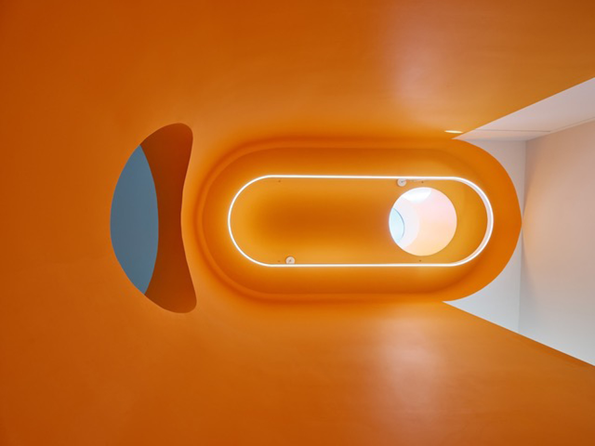 Futuristicky působící průchod v interiéru domu Riverhouse pracuje s výraznou oranžovou barvou, zaoblenými liniemi a skrytým osvětlením.