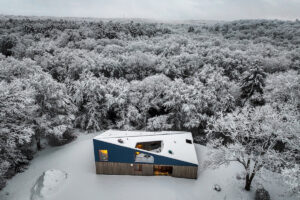 Rodinný dům Riverhouse zasazený do zasněžené krajiny kombinuje moderní architekturu s přírodními materiály a výraznou modrou střechou.