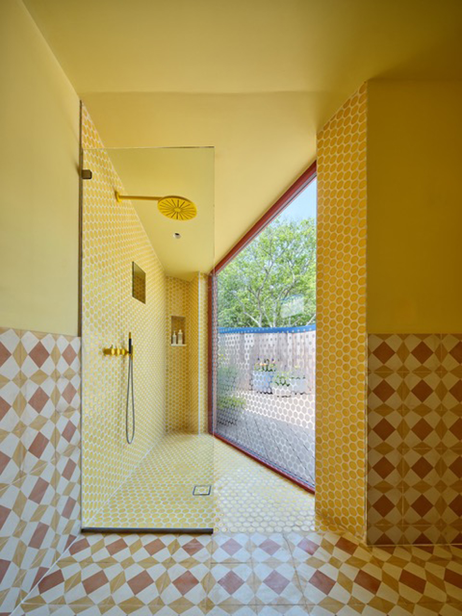 Designový sprchový kout v domě Riverhouse zaujme žlutými tóny, geometrickými obklady a velkým oknem propojujícím koupelnu s venkovním prostorem.