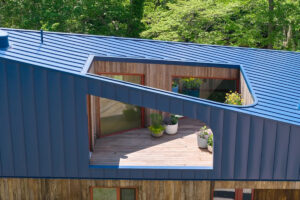 Střešní terasa domu Riverhouse je zapuštěná do výrazně tvarované modré střechy a vytváří soukromý venkovní prostor chráněný před okolím.
