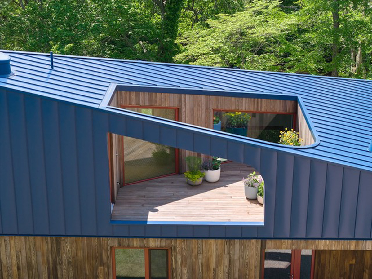 Střešní terasa domu Riverhouse je zapuštěná do výrazně tvarované modré střechy a vytváří soukromý venkovní prostor chráněný před okolím.