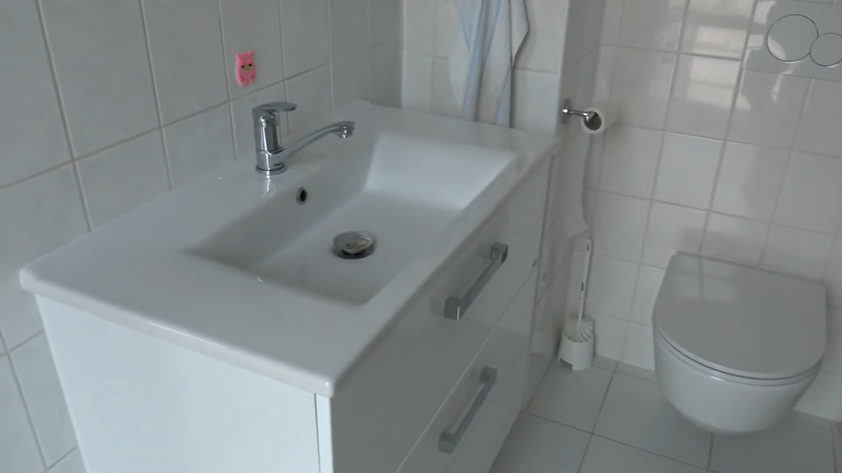 Moderní umyvadlo se skříňkou a závěsnou toaletou kontrastuje s původními bílými obklady v koupelně.