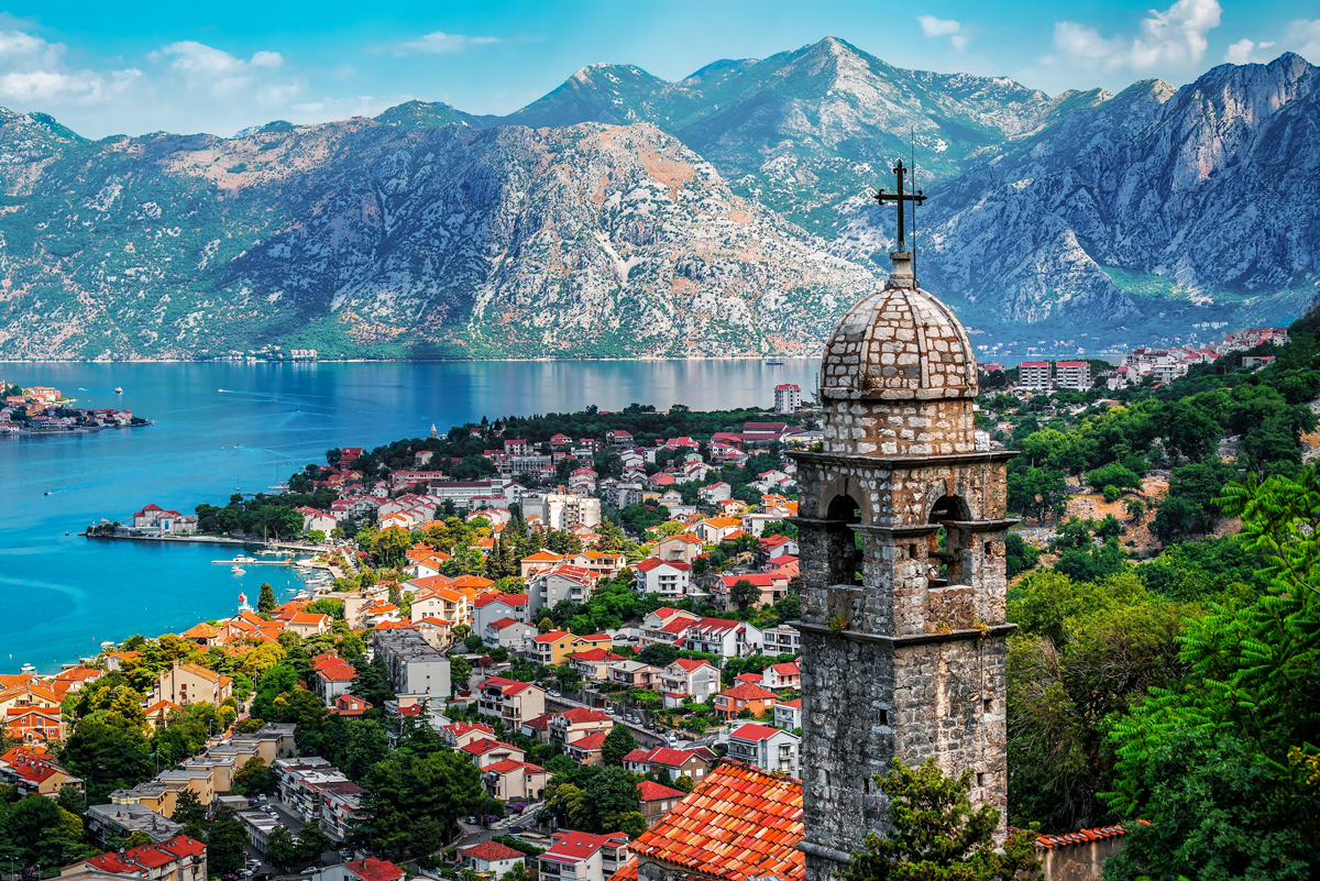 Pohled na historický Kotor v Černé Hoře s kostelní věží, Kotorským zálivem a horskými štíty v pozadí.