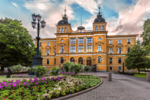 Historická budova radnice ve finském Oulu obklopená upravenými záhony a městským parkem.