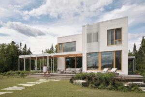 Bílá fasáda, velká okna a krytá veranda propojují moderní architekturu s klidnou krajinou kolem jezera.