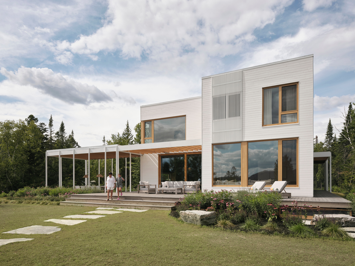 Bílá fasáda, velká okna a krytá veranda propojují moderní architekturu s klidnou krajinou kolem jezera.