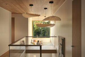 Chodba v patře vede kolem odpočinkové sítě zavěšené nad obytným prostorem a rámuje výhled do korun stromů.