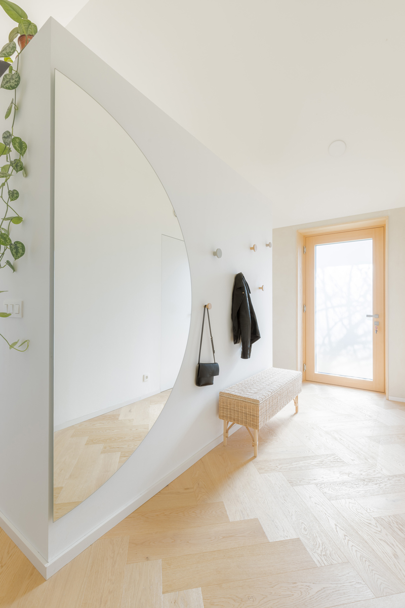 Minimalistická předsíň s velkoformátovým zrcadlem a světlou dubovou podlahou působí vzdušně a elegantně.