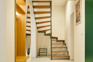 Zelené ocelové schodiště s dřevěnými nášlapy tvoří výrazný architektonický prvek propojující obě podlaží bytu.