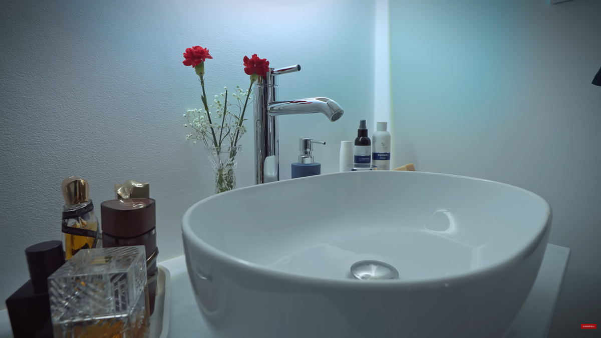 Detail koupelnového umyvadla ukazuje jednoduchý moderní design doplněný osobními dekoracemi a čerstvými květinami.
