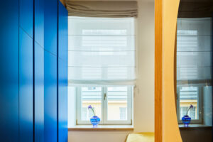 Výrazná modrá vestavěná skříň dodává ložnici energii a vytváří kontrast k teplé dřevěné podlaze i historickým okenním rámům.