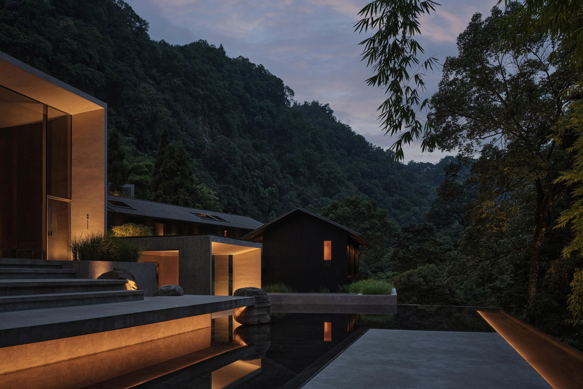 Večerně nasvícený bazén odráží minimalistickou architekturu resortu uprostřed horského lesa.