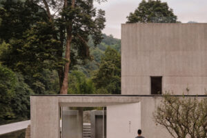 Vstup do resortu tvoří minimalistická betonová architektura zasazená mezi vzrostlé stromy a vysoké okrasné trávy.