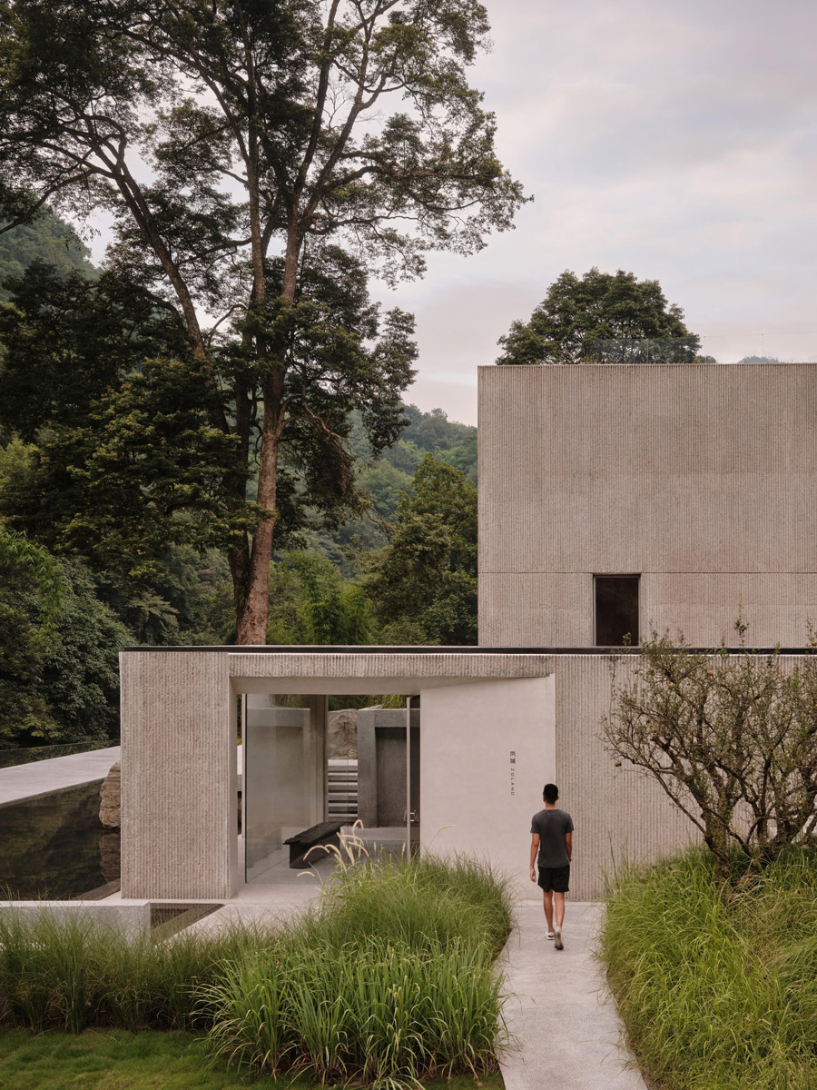 Vstup do resortu tvoří minimalistická betonová architektura zasazená mezi vzrostlé stromy a vysoké okrasné trávy.