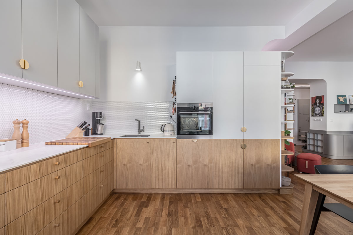 Minimalistická kuchyň spojuje světlé horní skříňky s dubovou dýhou a navazuje na vestavěnou knihovnu v denní zóně.