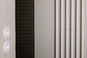 Detail keramického obkladu v koupelně s kontrastními světlými a tmavými dlaždicemi a designovým radiátorem.
