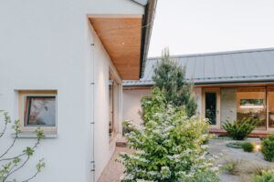 Boční pohled ukazuje jednoduchou architekturu domu s přírodními materiály a propojením se zahradou.