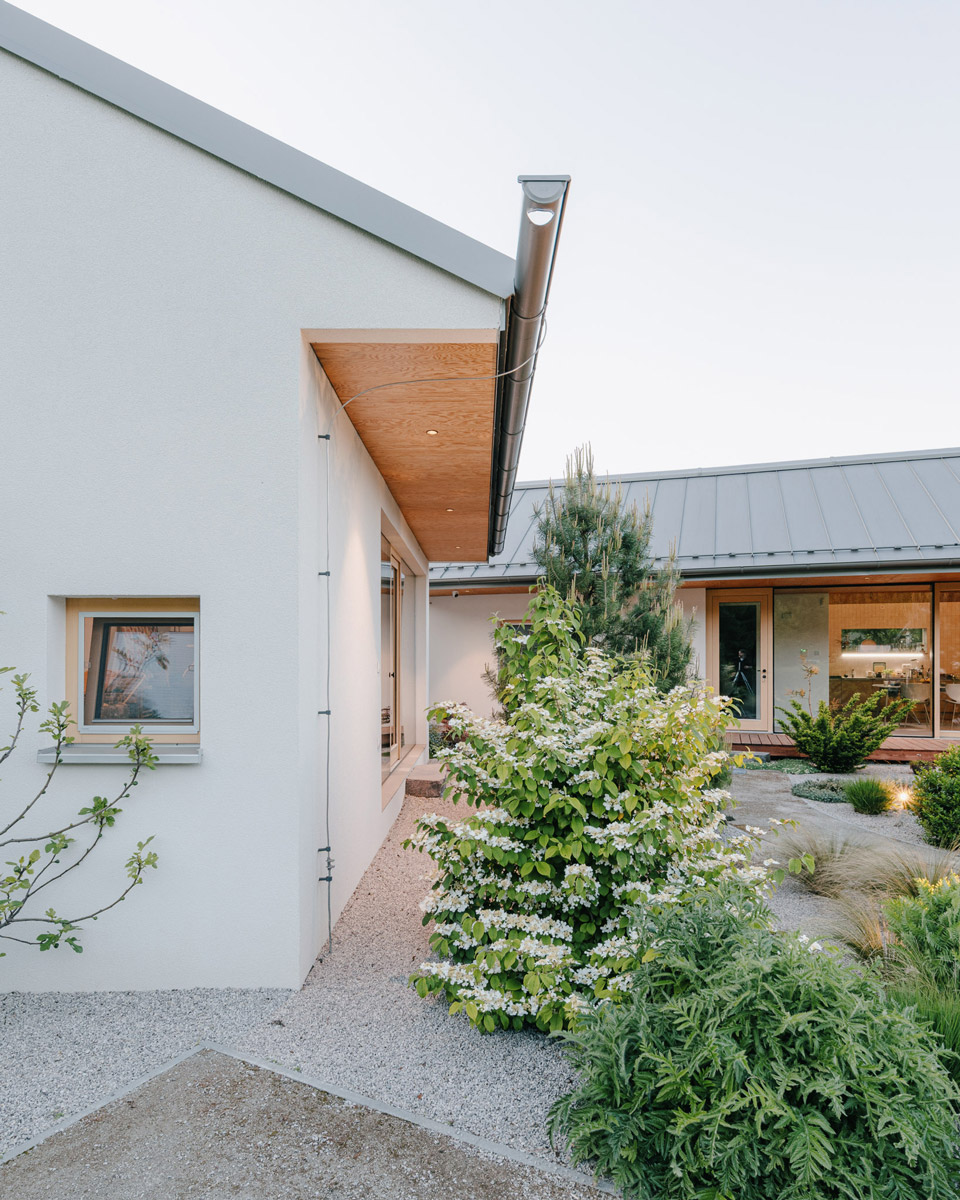 Boční pohled ukazuje jednoduchou architekturu domu s přírodními materiály a propojením se zahradou.