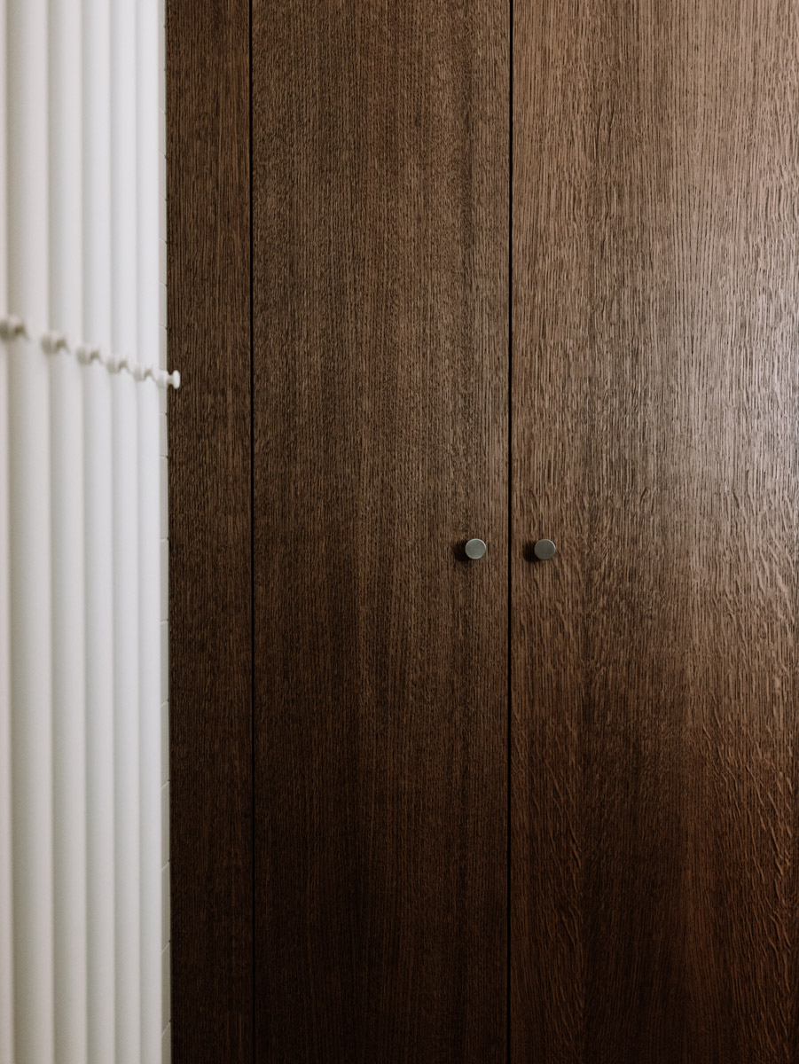 Detail vestavěné skříně z tmavě mořeného dubového dřeva s minimalistickými úchytkami.