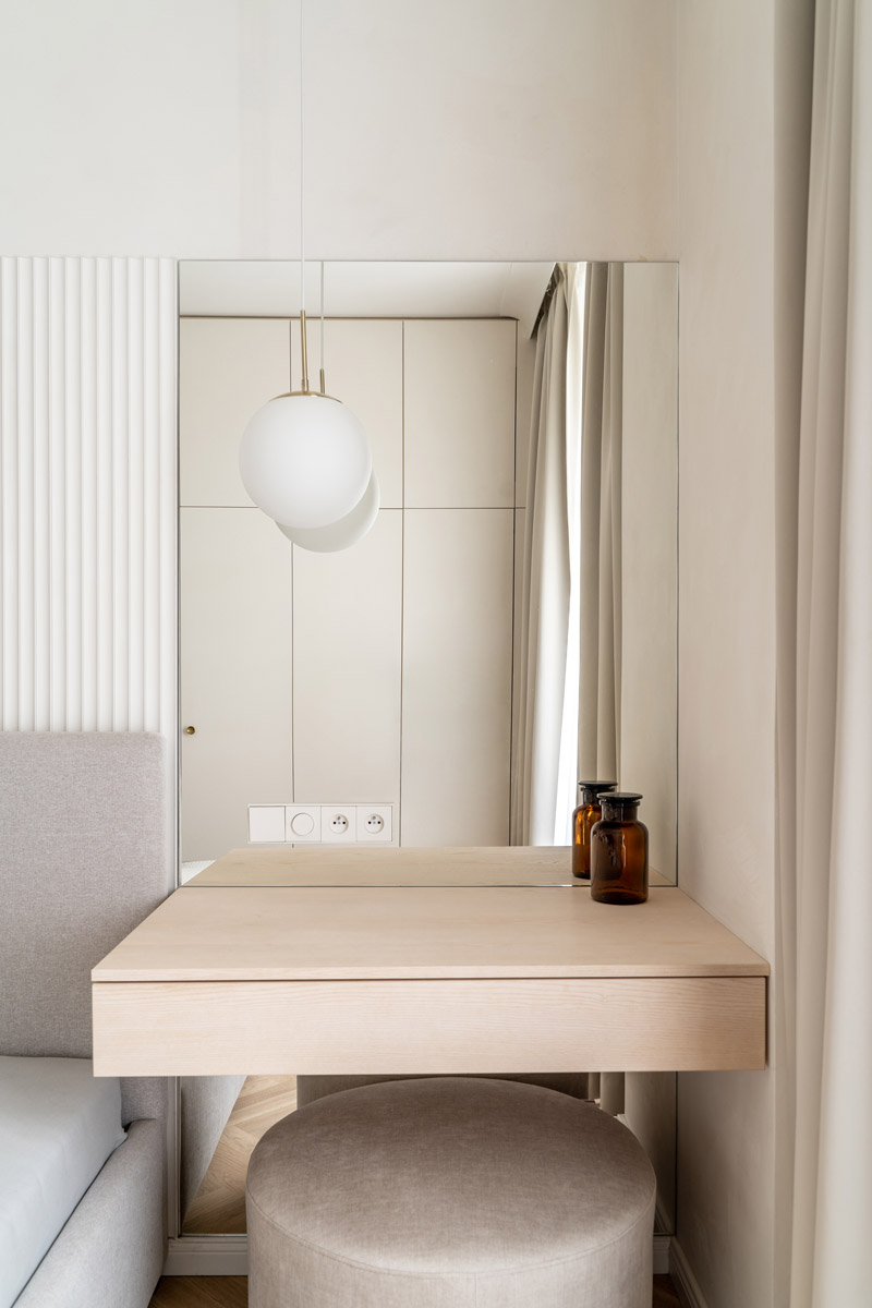 Minimalistický toaletní stolek navazuje na čelo postele a díky velkému zrcadlu i světlým materiálům podporuje vzdušnou atmosféru ložnice.