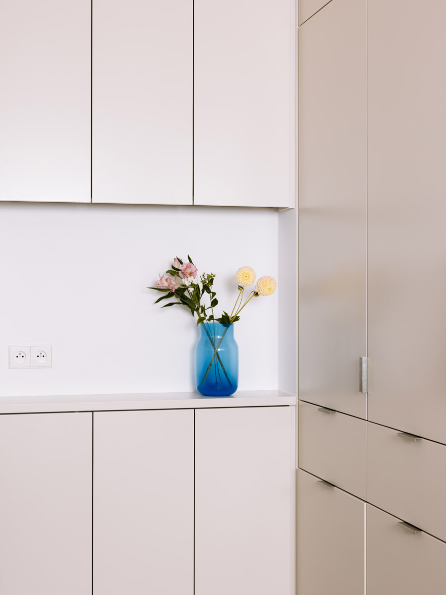 Detail kuchyňské sestavy v odstínu off white doplněné modrou skleněnou vázou s květinami.