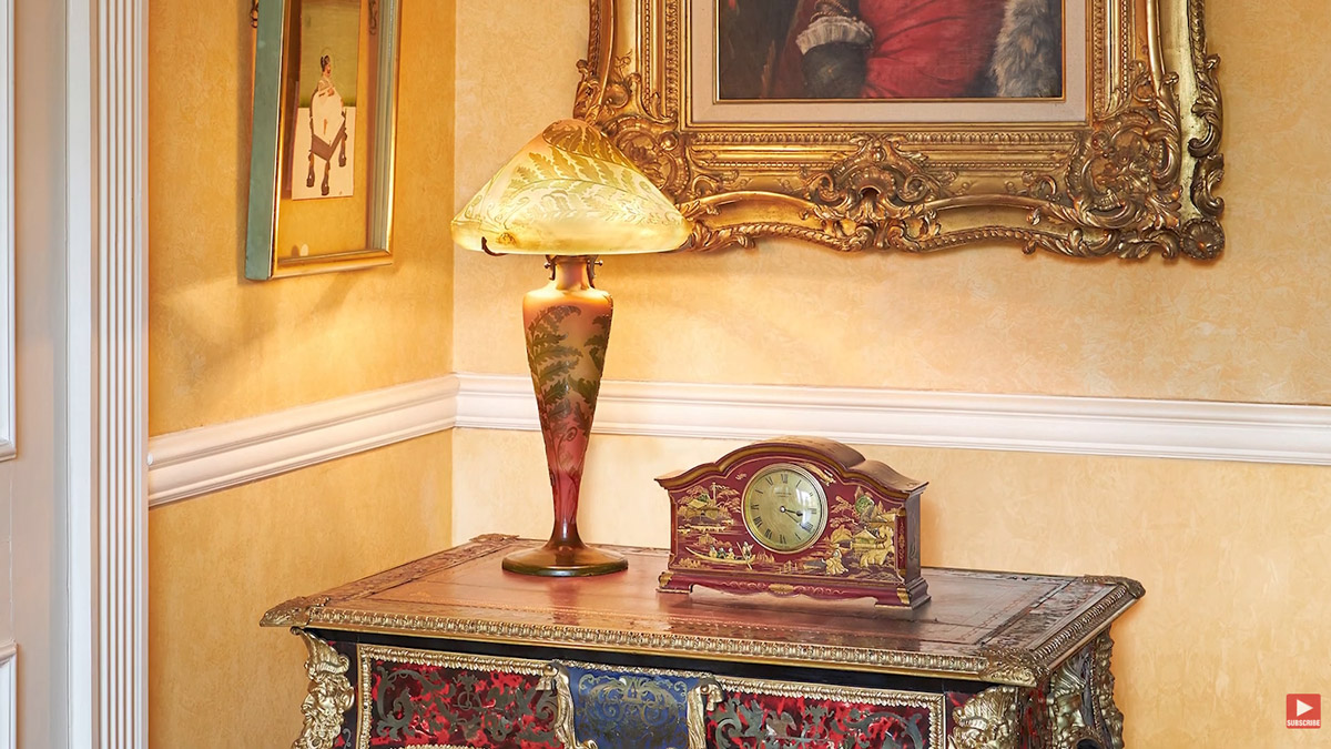 Historický stolek, dekorativní lampa a starožitné hodiny dotvářejí elegantní atmosféru interiéru.