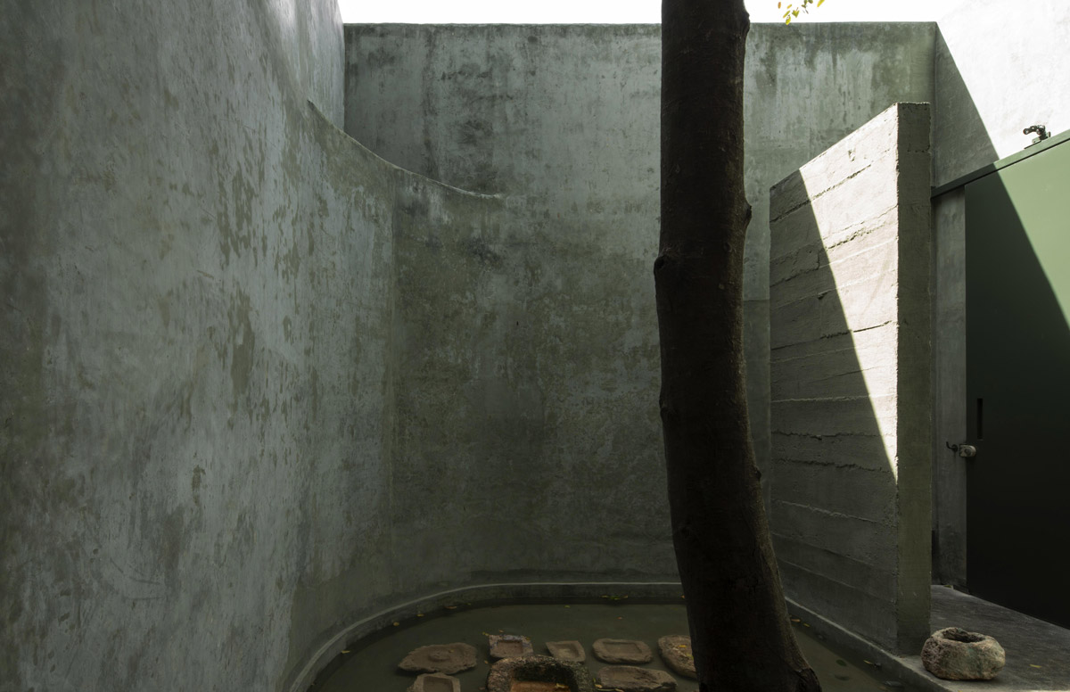 Betonové atrium se vzrostlým stromem a mělkým vodním prvkem v rezidenci Casa Gruta.