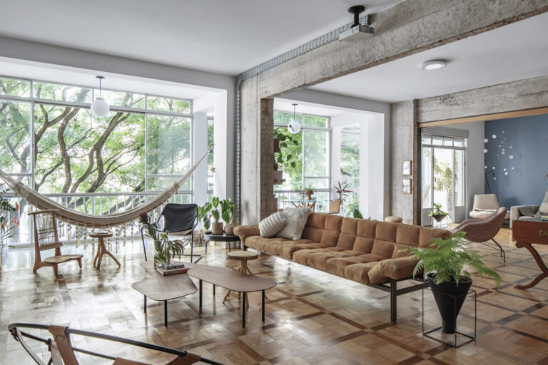Prostorná denní zóna penthousu s houpací sítí, designovým nábytkem, původními parketami, velkými okny a přiznanou betonovou konstrukcí.