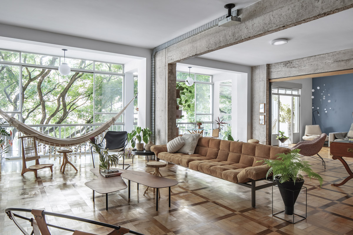 Prostorná denní zóna penthousu s houpací sítí, designovým nábytkem, původními parketami, velkými okny a přiznanou betonovou konstrukcí.