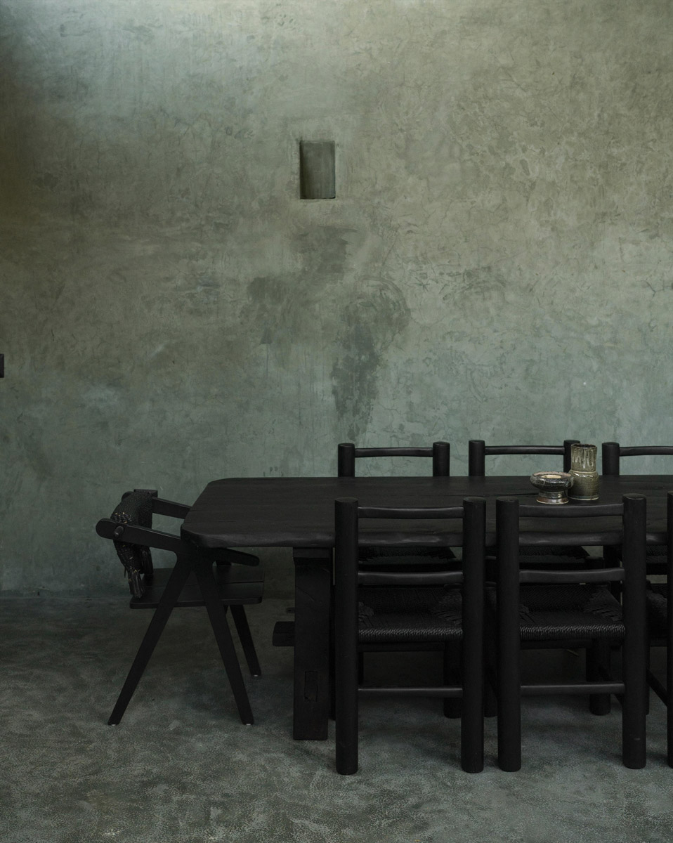 Černý jídelní stůl a židle před surovou betonovou stěnou v minimalistickém interiéru Casa Gruta.