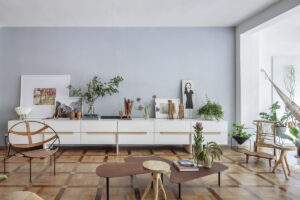 Obývací pokoj s původní dřevěnou podlahou, dlouhou bílou komodou, uměleckými díly, rostlinami a designovým nábytkem.