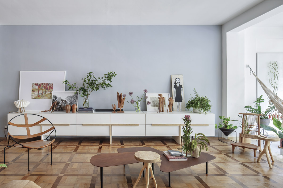Obývací pokoj s původní dřevěnou podlahou, dlouhou bílou komodou, uměleckými díly, rostlinami a designovým nábytkem.