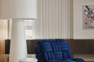 Modré křeslo spletené z lana doplňuje výrazná stojací lampa a terrazzový stolek, které tvoří hlavní designové akcenty interiéru.
