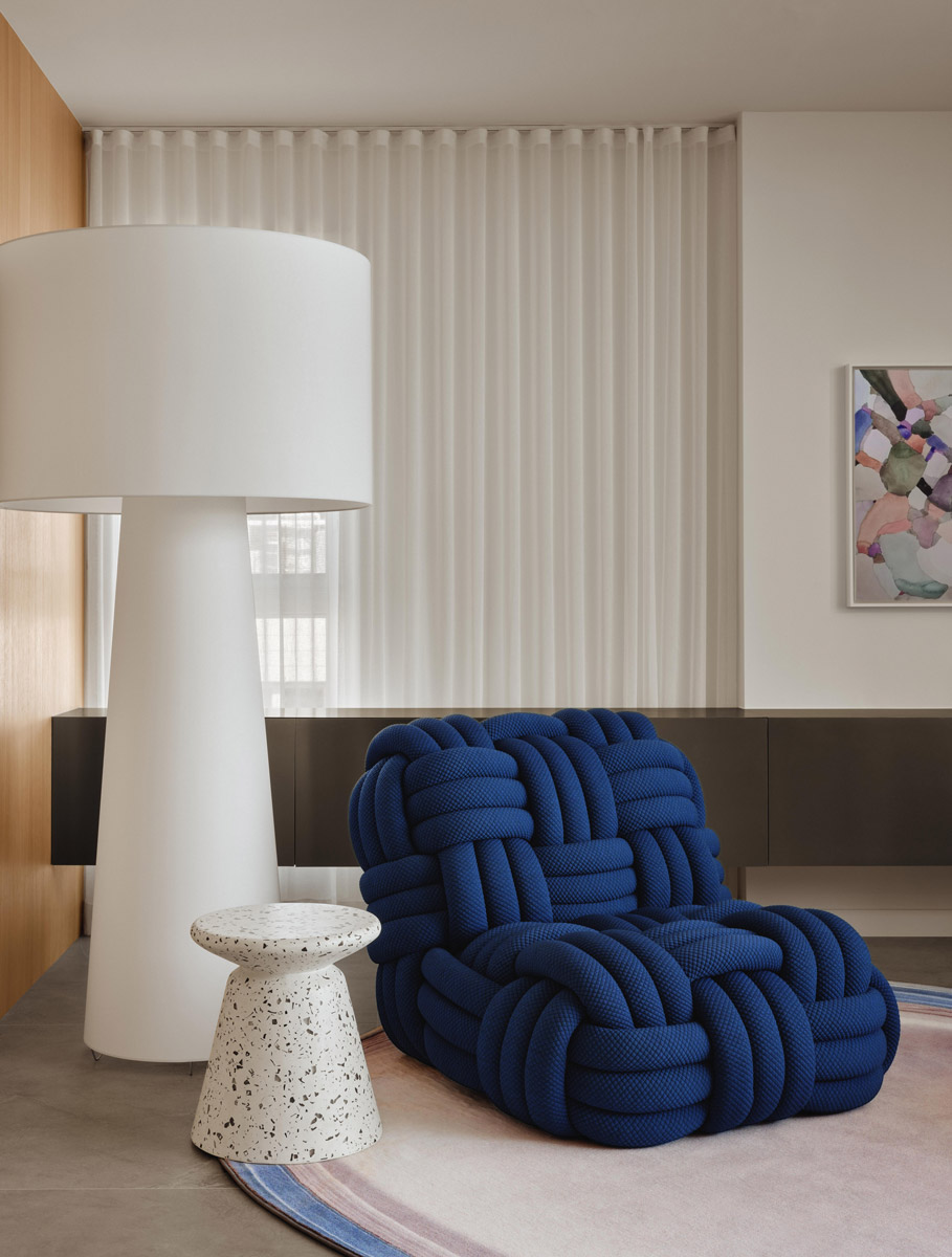 Modré křeslo spletené z lana doplňuje výrazná stojací lampa a terrazzový stolek, které tvoří hlavní designové akcenty interiéru.