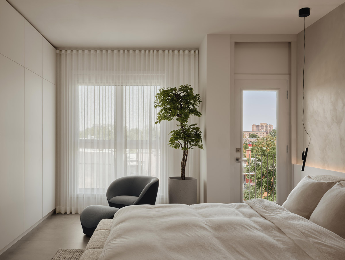 Světlá ložnice s velkým oknem, pohodlným křeslem a přístupem na balkon působí vzdušně a klidně.